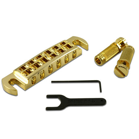 Gold wraparound guitar bridge with two knurled posts, an Allen wrench, and a black adjustment wrench on a white background.