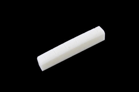 White slotted bone nut for acoustic guitar on a black background.