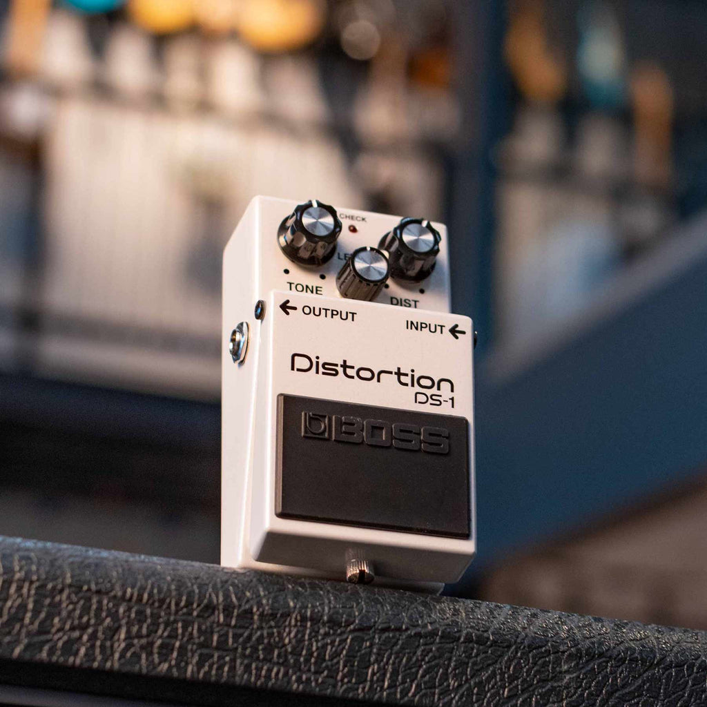 White distortion guitar pedal with three control knobs and input/output jacks on a textured surface.