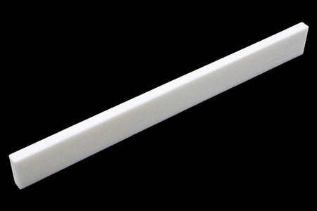 White rectangular bone or synthetic guitar saddle blank on a black background.