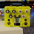 Yellow guitar effects pedal with multiple knobs, two toggle switches, two footswitches, and cartoon shower graphic.