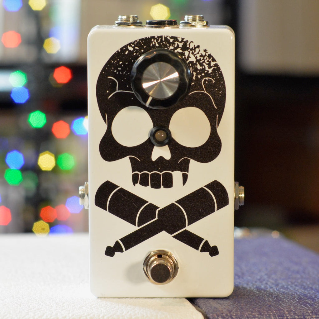 White guitar pedal with black skull and crossed 1/4 inch plug graphics, one knob, one foot switch, and two audio jacks.