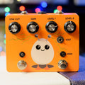 Orange guitar effects pedal with four control knobs, two footswitches, a toggle switch, and a cartoon egg character graphic.