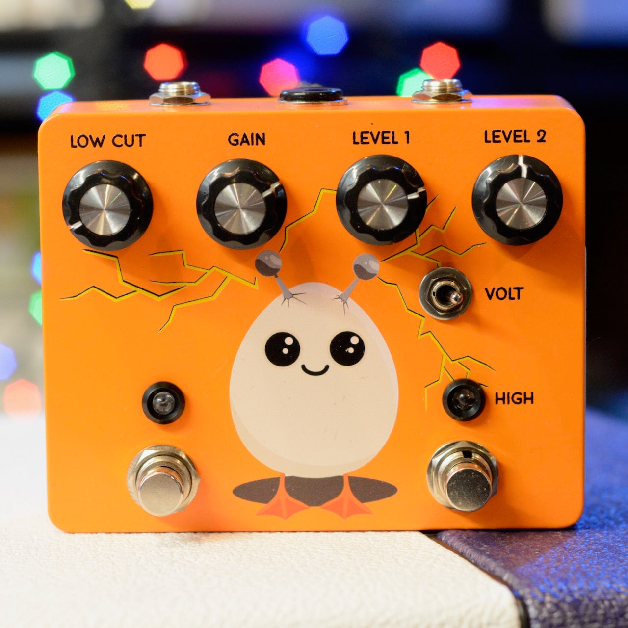Orange guitar effects pedal with four control knobs, two footswitches, a toggle switch, and a cartoon egg character graphic.