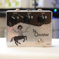 Silver guitar pedal with three black knobs labeled Output, Treble, Gain, a footswitch, and a centaur clown graphic.