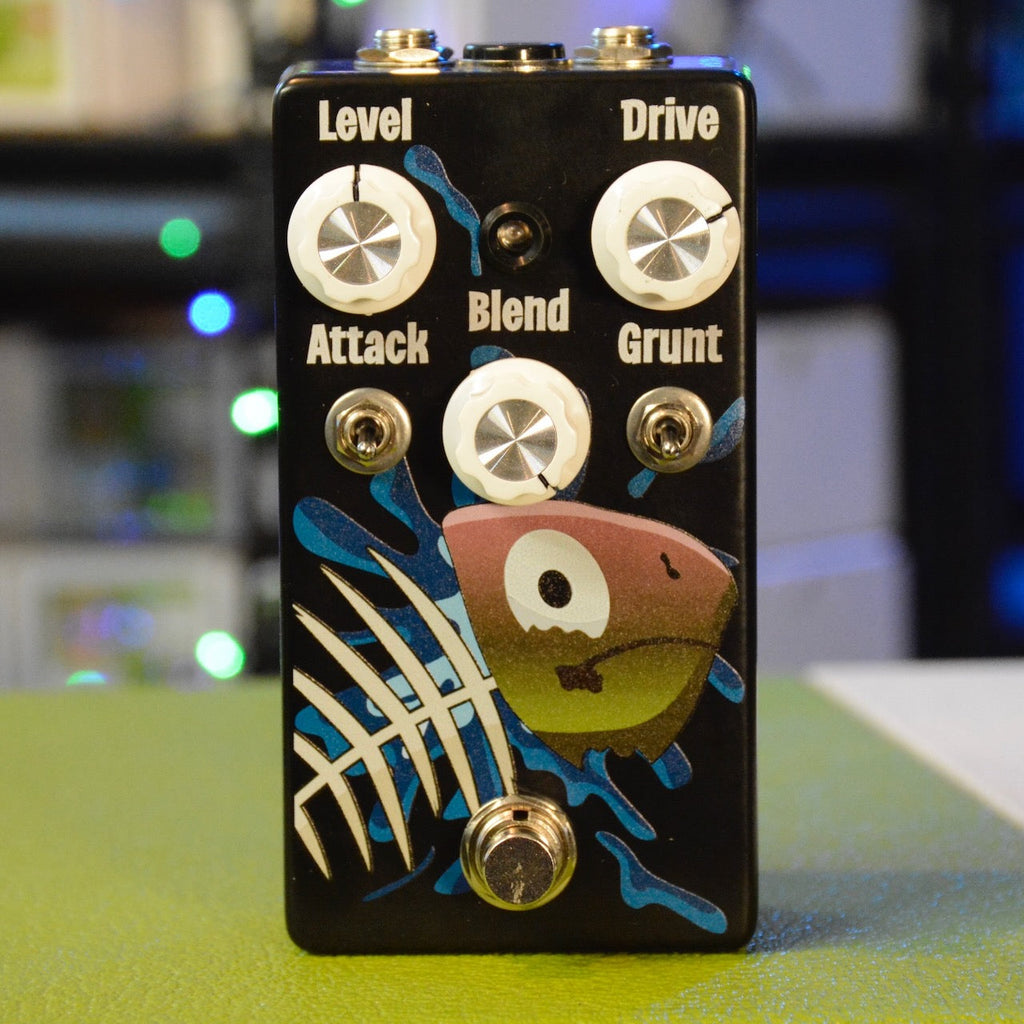 Black guitar effects pedal with fish graphic and five control knobs labeled Level, Drive, Attack, Blend, and Grunt plus two toggle switches and a footswitch.