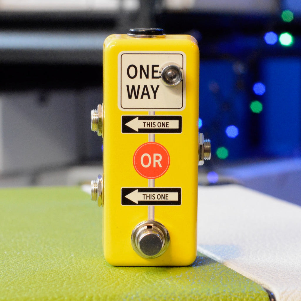 Yellow rectangular guitar pedal with footswitch, three 1/4 inch jacks and directional labels on the front.