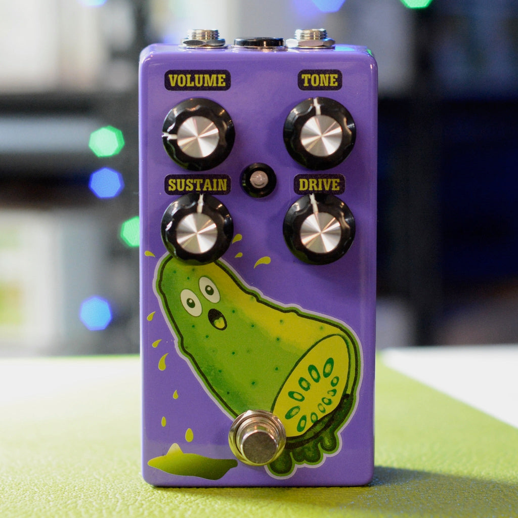 Purple guitar effects pedal with four control knobs, a footswitch, and a cartoon pickle graphic on the front.