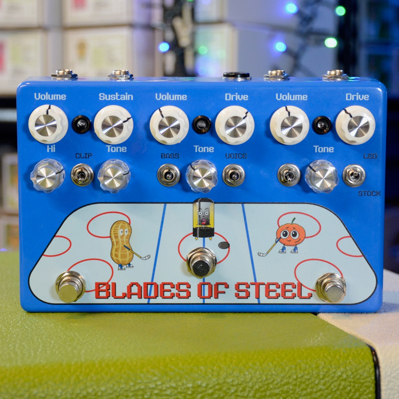 Blue guitar effects pedal with multiple knobs, toggle switches, footswitches, and cartoon characters on a hockey rink graphic.