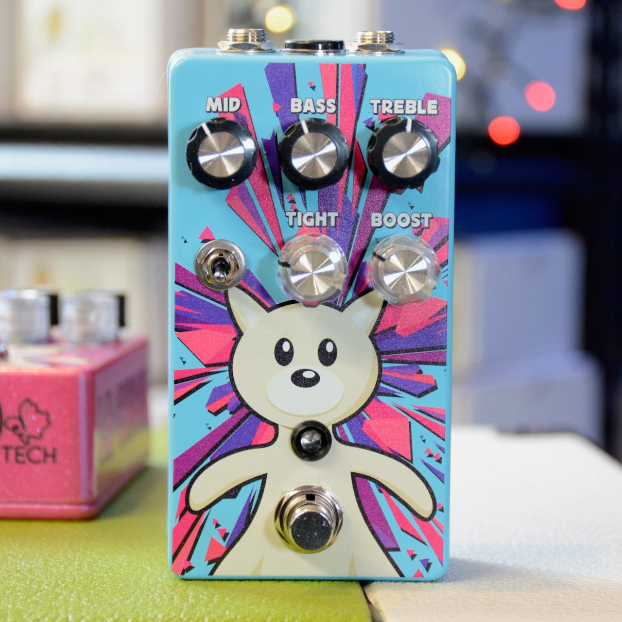 Blue guitar effects pedal with cartoon bear graphic and five knobs labeled mid, bass, treble, tight, and boost.