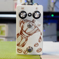 White guitar pedal with coffee pot graphic and coffee beans, two knobs labeled IN and OUT, a toggle switch, and a footswitch.