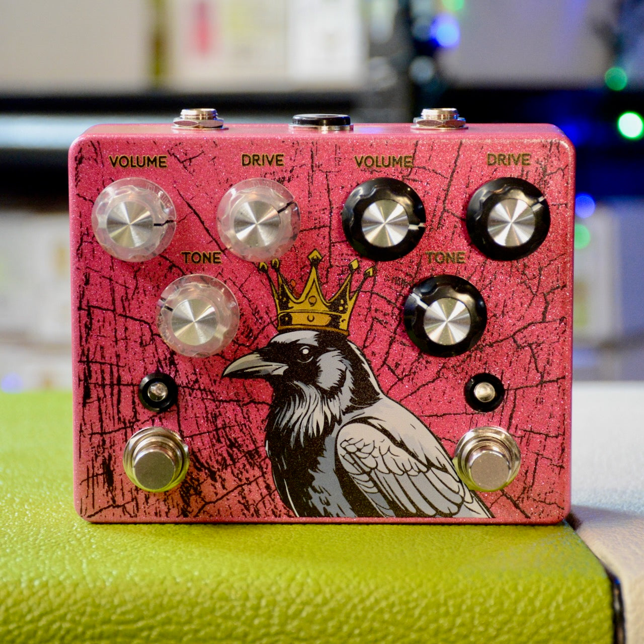 Pink guitar effects pedal with a crowned crow graphic and two sets of volume, drive, and tone knobs with footswitches.