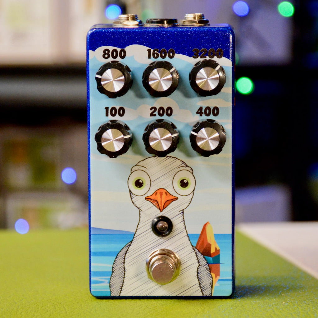 Blue guitar pedal with six rotary knobs labeled with frequency numbers and a foot switch, featuring a cartoon bird graphic.