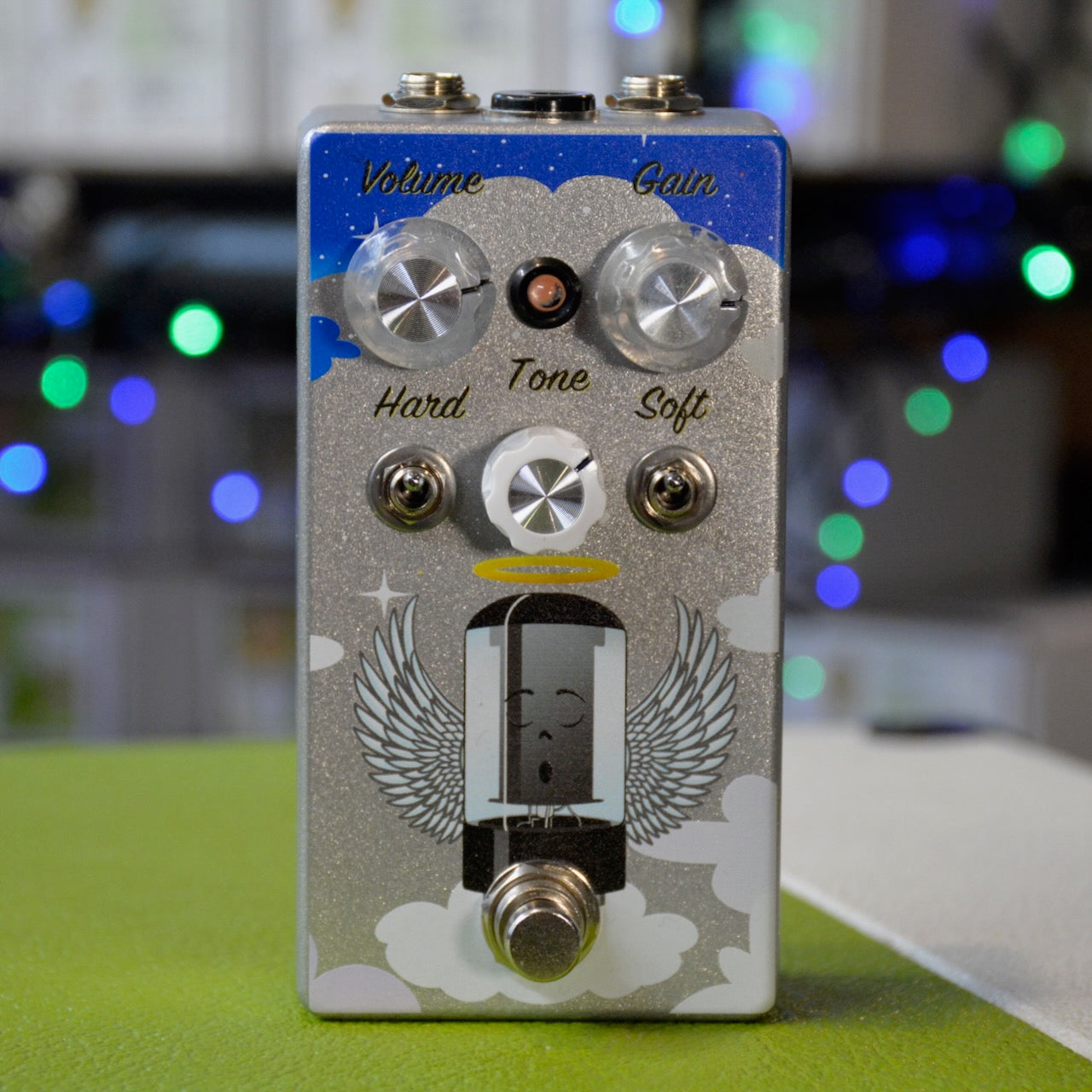 Guitar effects pedal with knobs for Volume, Gain, Tone, two toggle switches, and a footswitch with angel wings artwork.