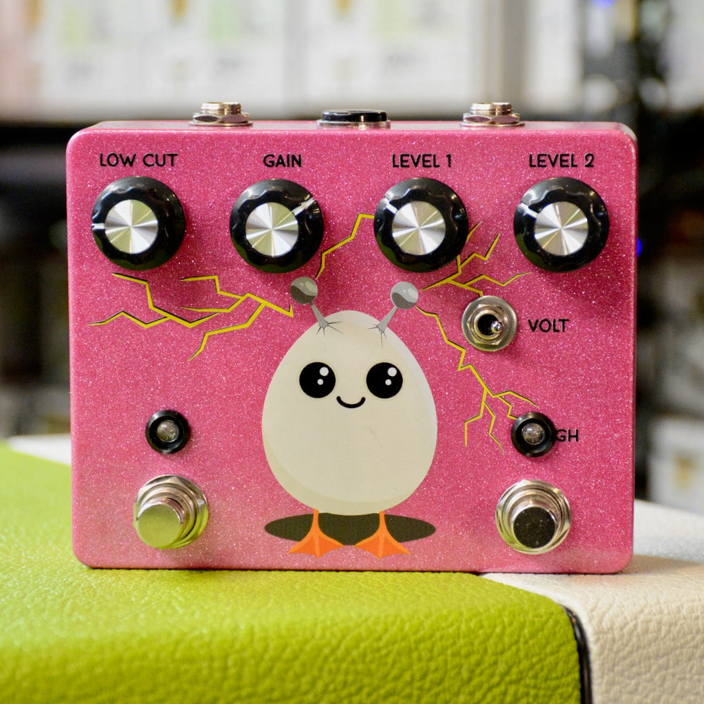 Pink effects pedal with four knobs, two footswitches, two jacks on top, toggle switch, and cartoon chick illustration.