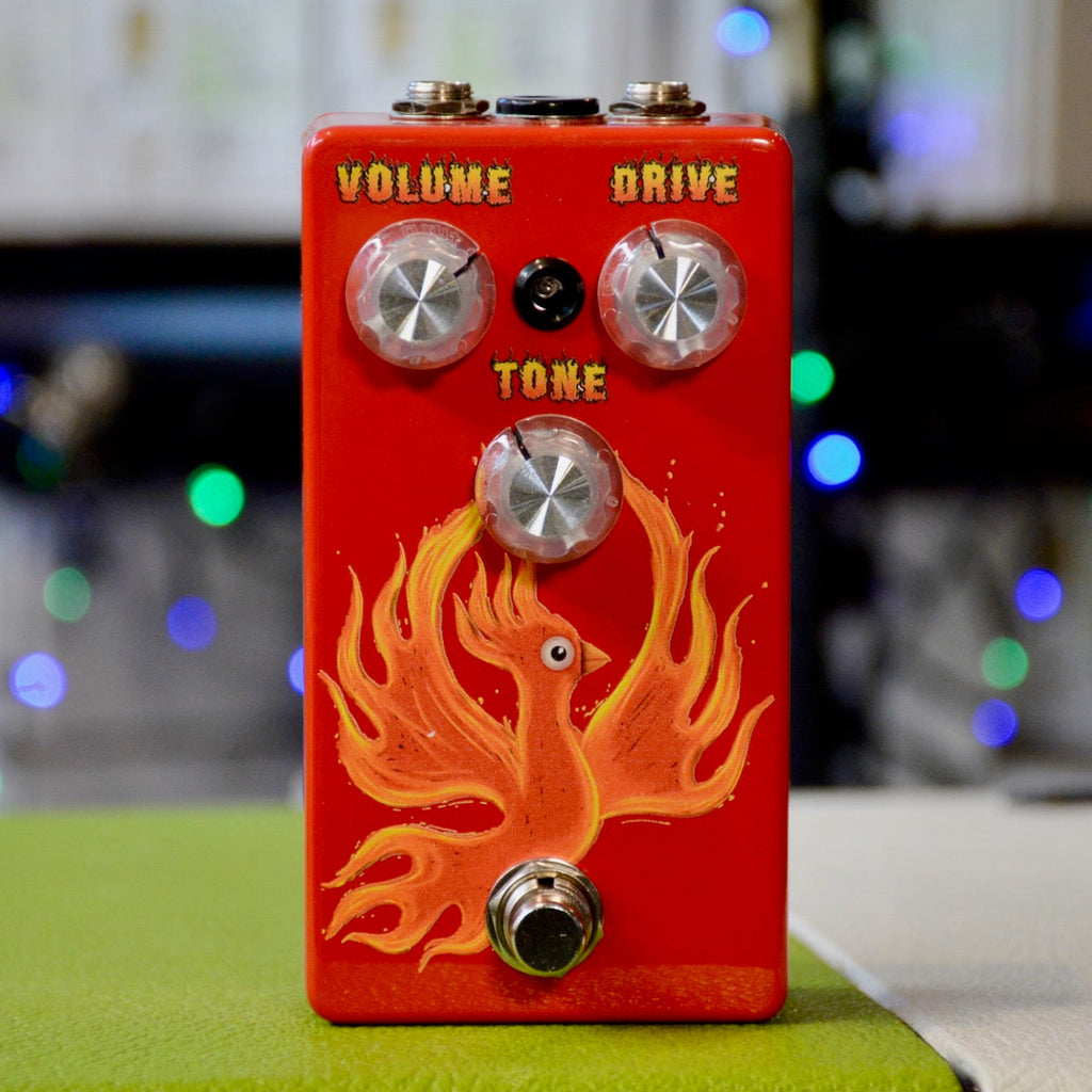 Red guitar effects pedal with phoenix graphic and three control knobs labeled Volume, Drive, and Tone