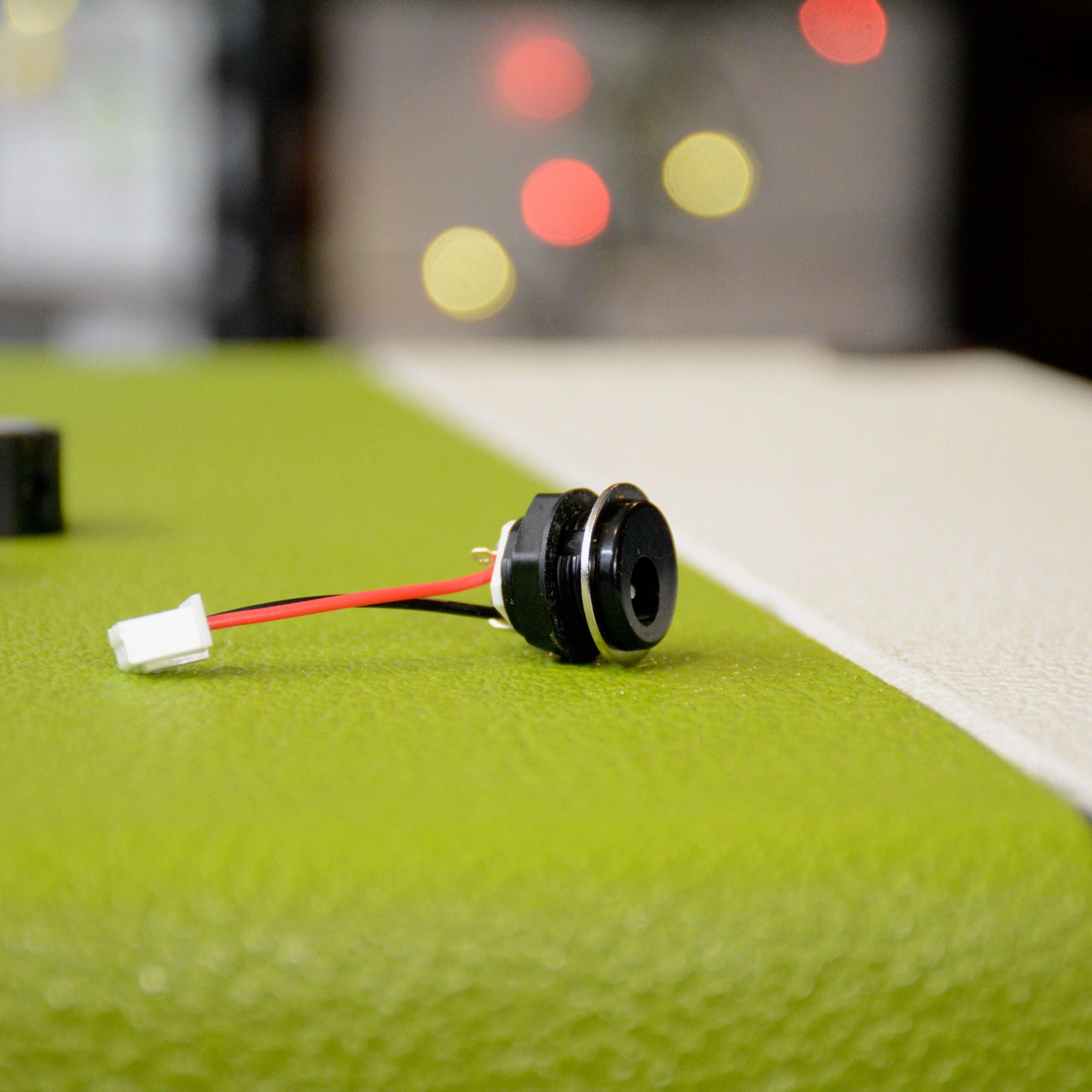 Black circular jack assembly with metal ring and red and black wires connected to white plastic connector on green surface.
