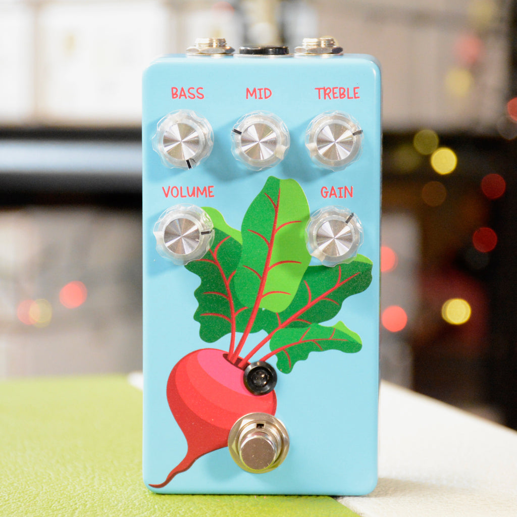 Light blue guitar effects pedal with bass, mid, treble, volume, and gain knobs and a red beet illustration.