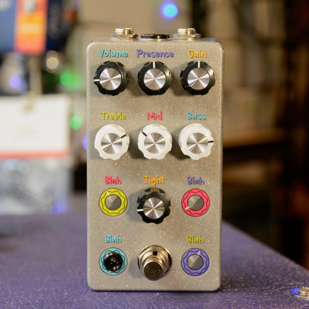 Silver guitar effect pedal with multiple rotary knobs labeled Volume, Presence, Gain, Treble, Mid, Bass, Blah, and Tight, plus a footswitch and audio jacks.