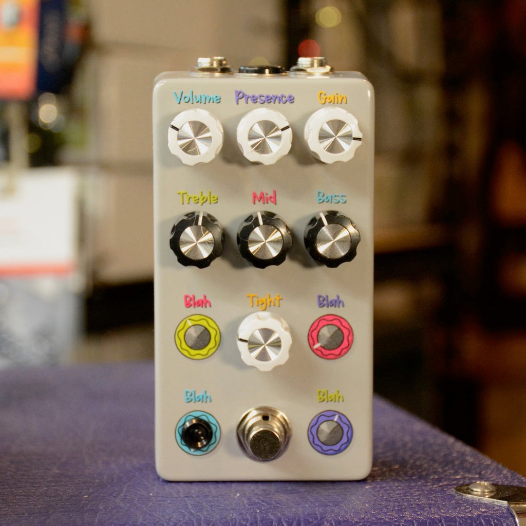 White guitar effects pedal with multiple labeled knobs and a footswitch placed on a textured surface.
