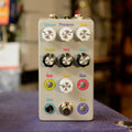 White guitar effects pedal with multiple labeled knobs and a footswitch placed on a textured surface.