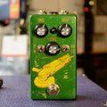 Green pedal with three knobs, two toggle switches, and a footswitch, featuring an illustration of a yellow angle grinder.