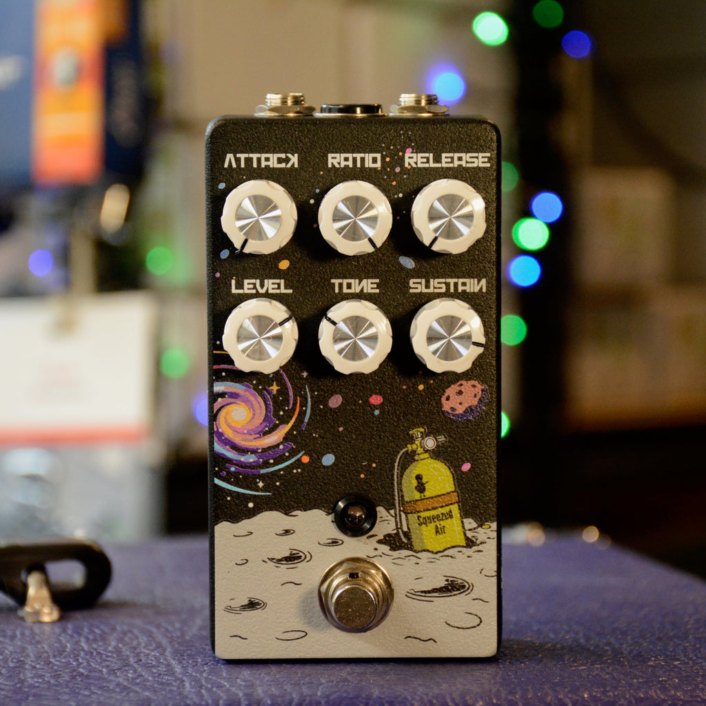 Black guitar effects pedal with six white knobs labeled for compressor settings and a footswitch on space-themed artwork.