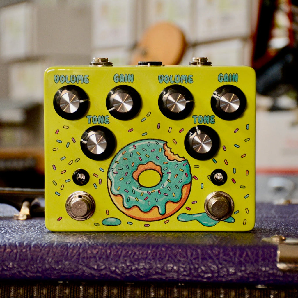 Yellow guitar pedal with two sets of Volume, Gain, Tone knobs and donut artwork in the center.