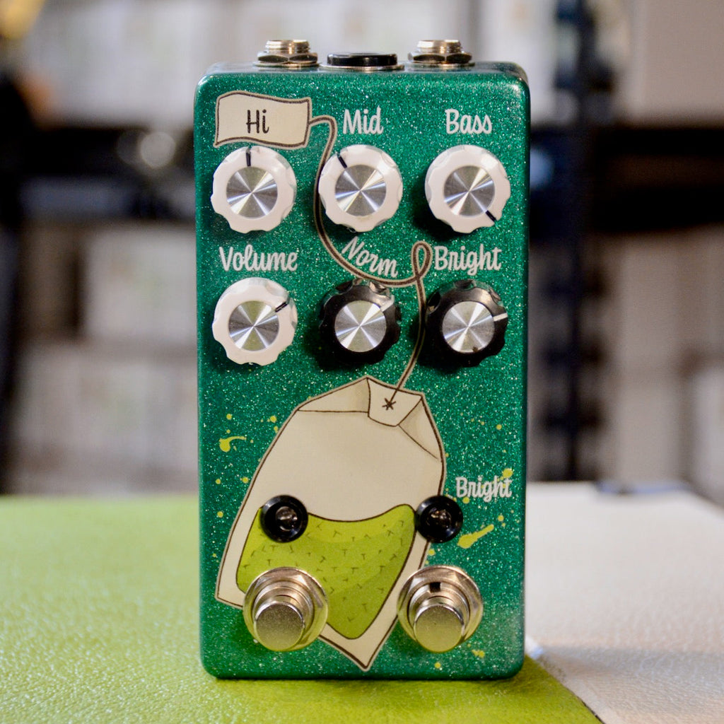 Green guitar effects pedal with six control knobs, two footswitches, and decorative tea bag graphic.