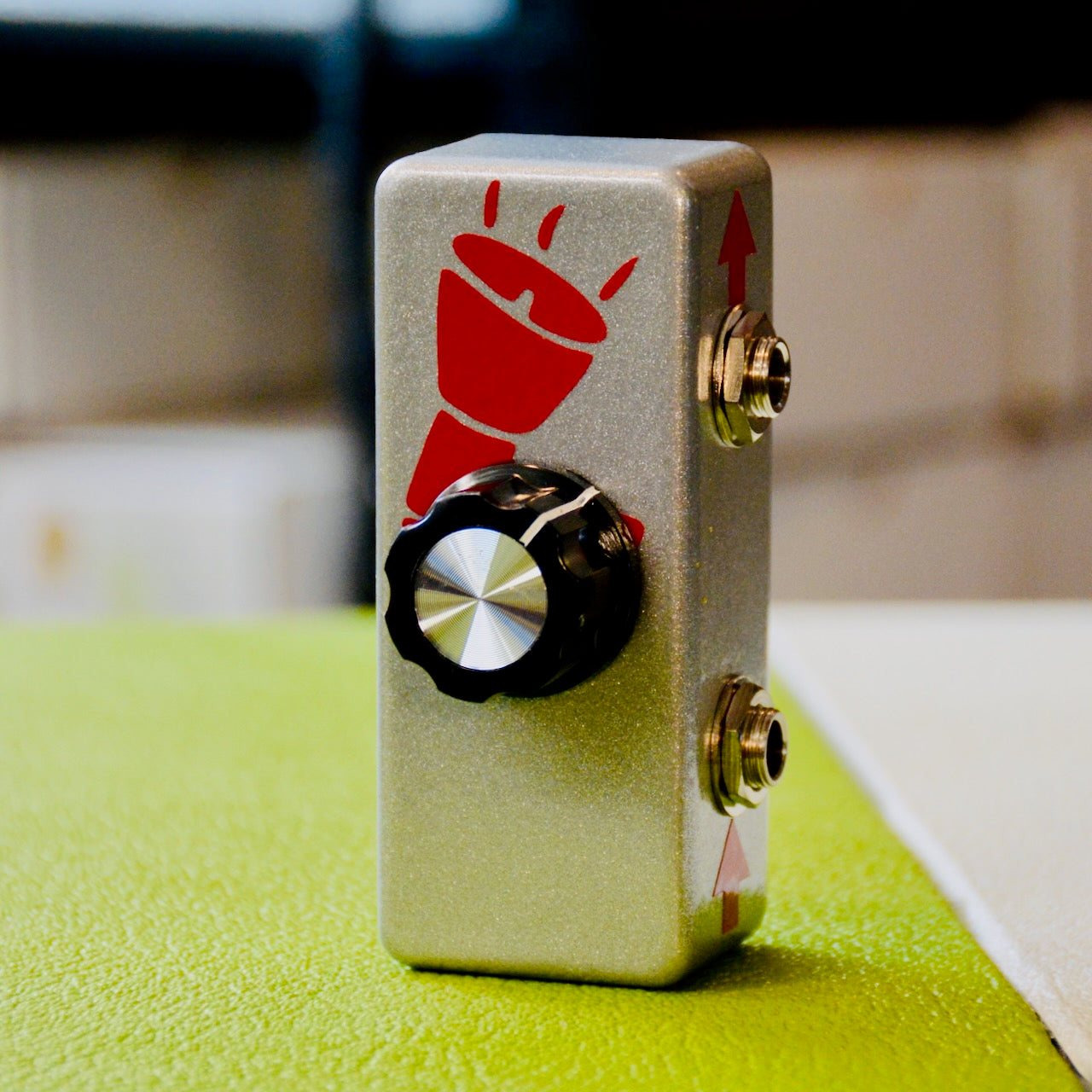 Silver rectangular device with black rotary knob and two audio jacks on the side with red graphics.