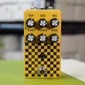 Gold and black checker patterned pedal with six knobs and a footswitch on front.
