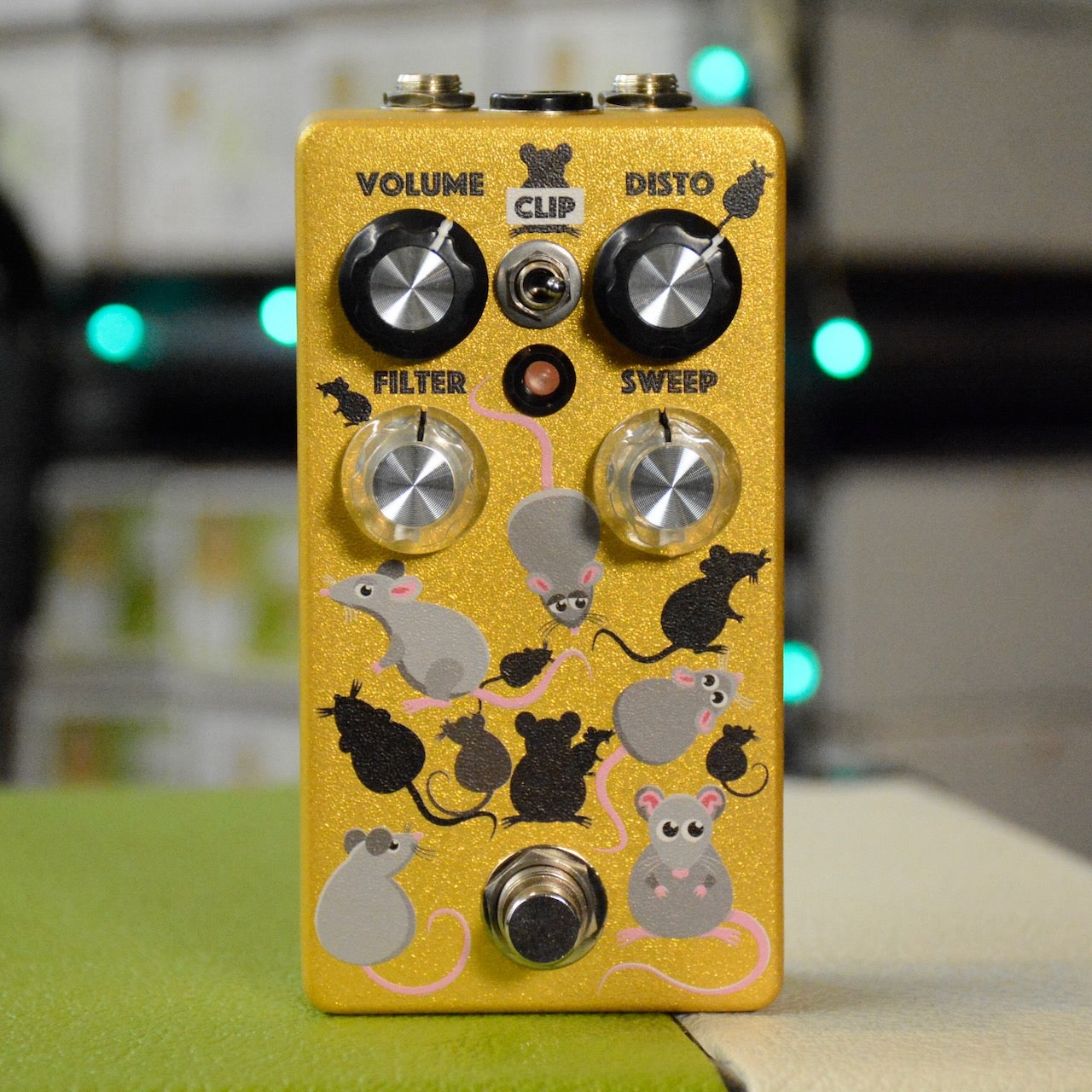 Gold-colored guitar effects pedal with four control knobs, one toggle switch, one footswitch, and mouse graphics.