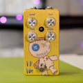 Gold-colored guitar effects pedal with four control knobs, a footswitch, and a voodoo doll graphic.