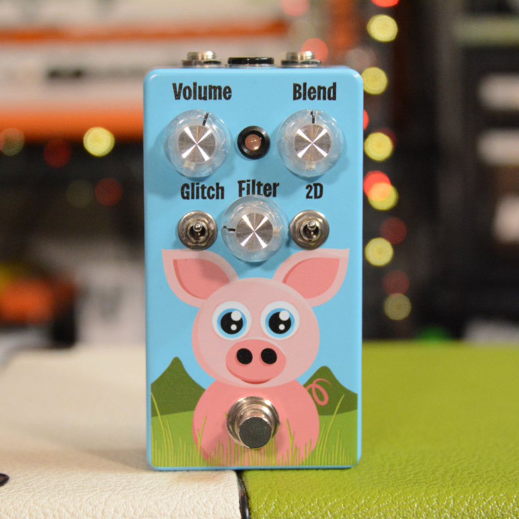 Light blue guitar pedal with a pig illustration, three knobs labeled Volume, Blend, and Filter, two toggle switches, and one footswitch.