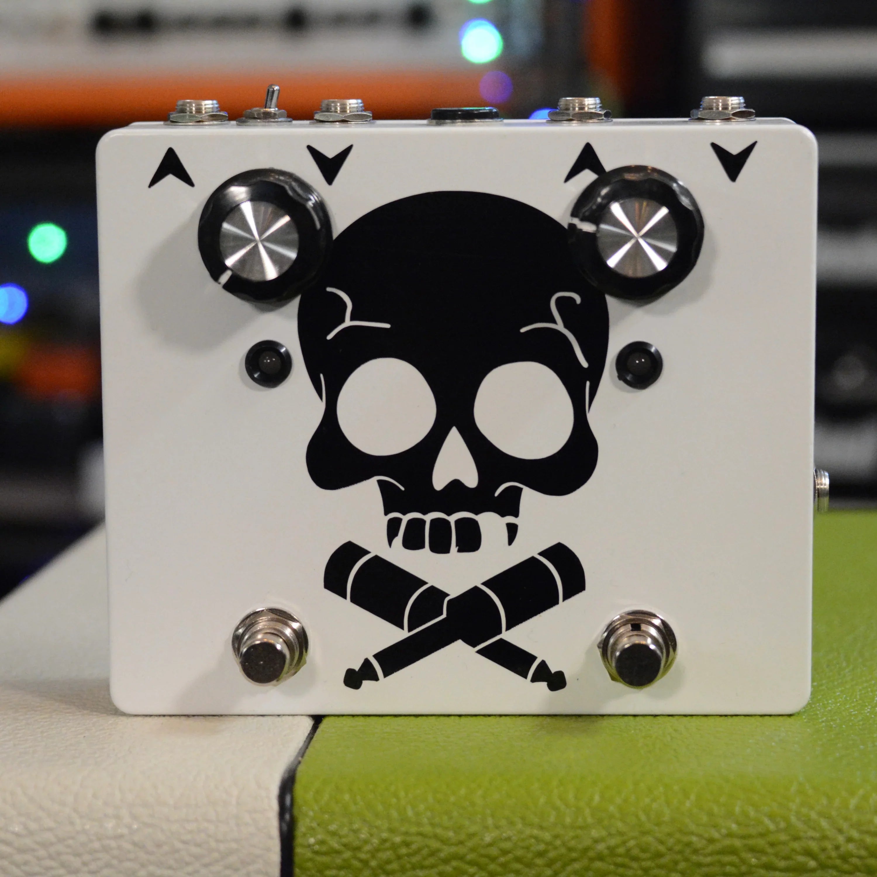White guitar effects pedal with black skull and crossed cables graphic, two knobs, two footswitches, and four quarter-inch jacks on top.