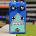 Blue guitar pedal with shark face graphic, two knobs labeled Volume and Gain, and a footswitch.