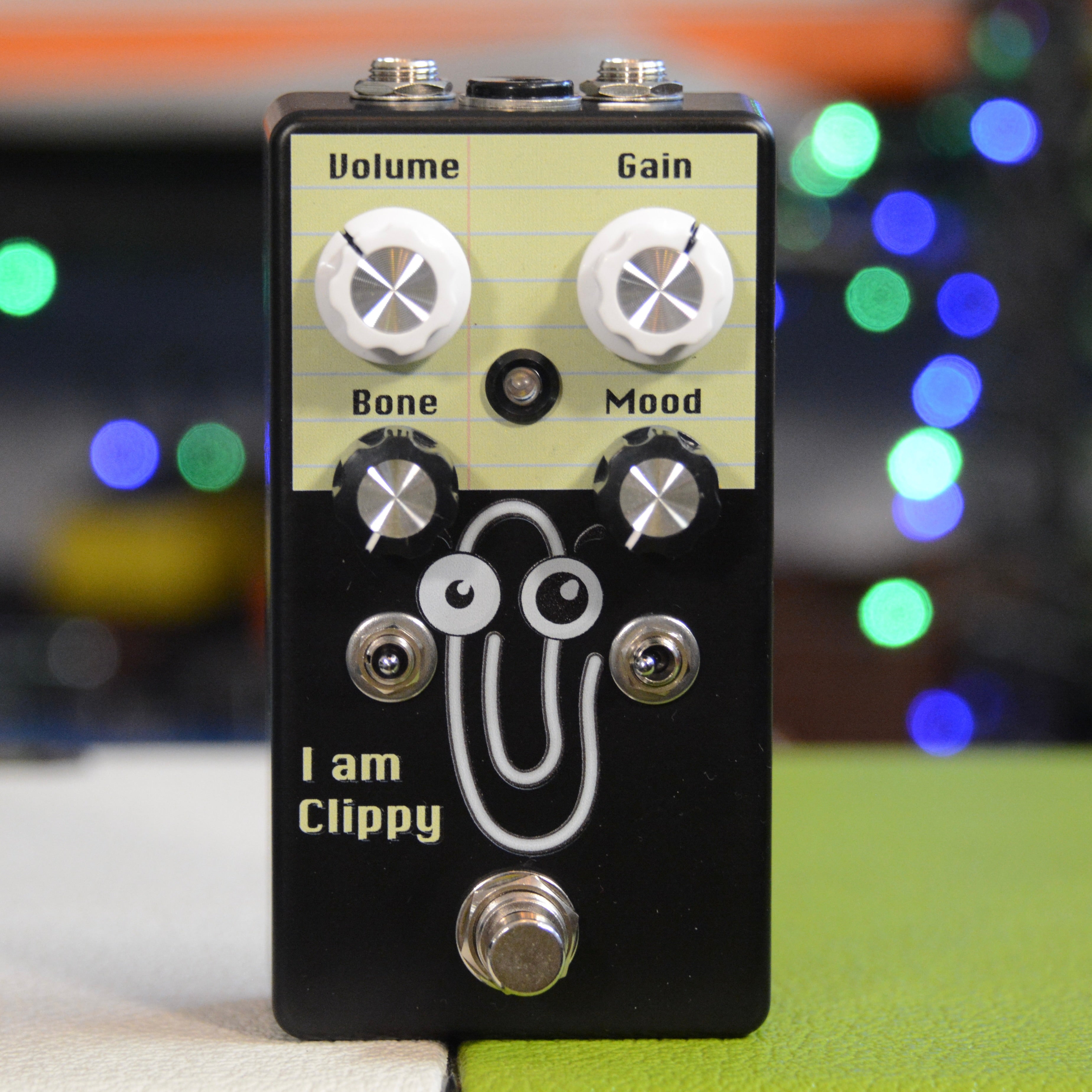 Black guitar effects pedal with four knobs, two toggle switches, one footswitch, and a cartoon paperclip graphic.