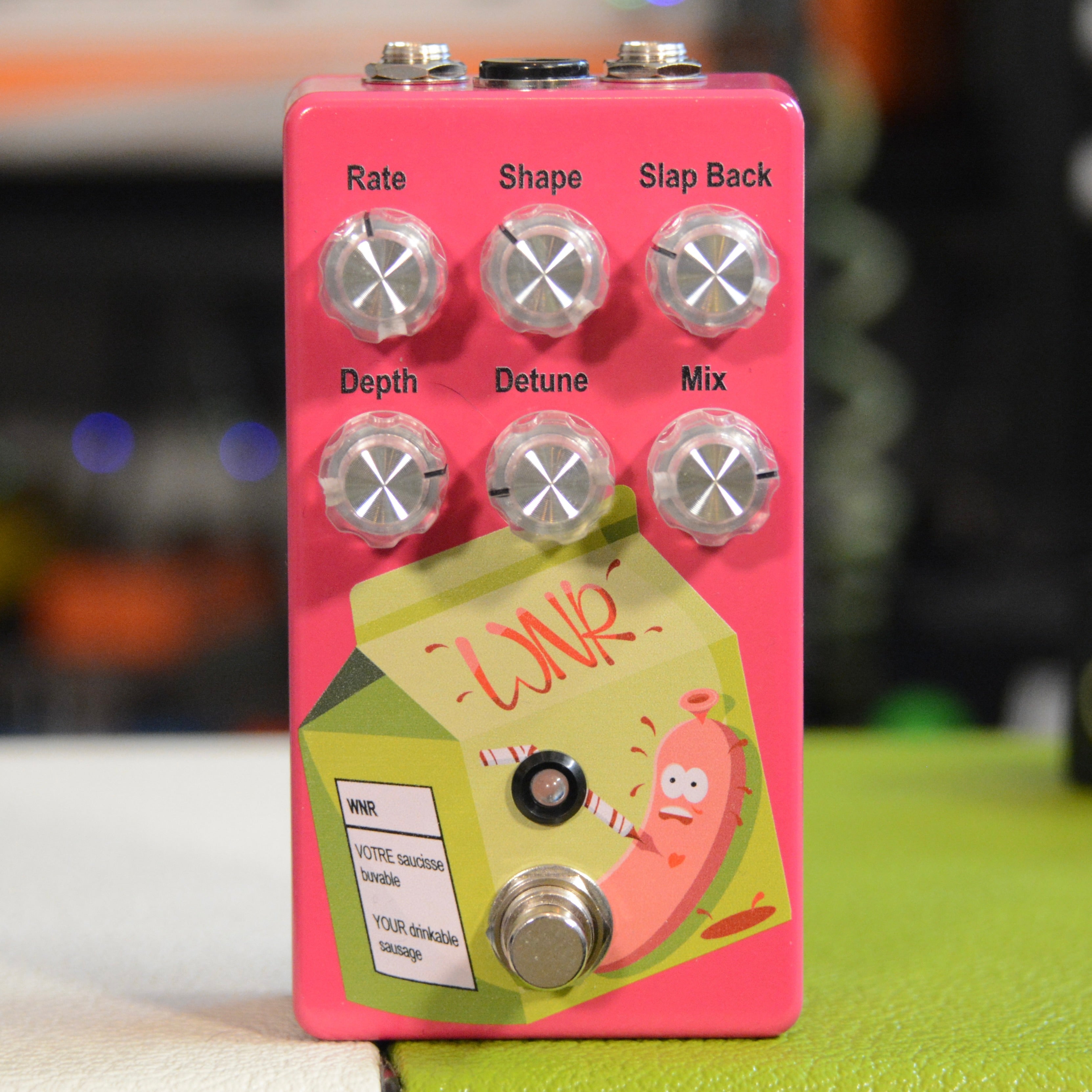 Pink guitar effects pedal with six control knobs, one footswitch, and a graphic of a sausage on a carton design.