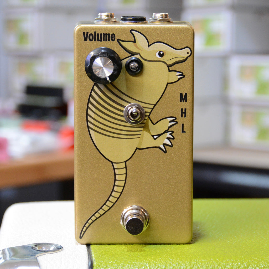 Gold-colored guitar effects pedal with armadillo graphic, a volume knob, a toggle switch, and a footswitch.