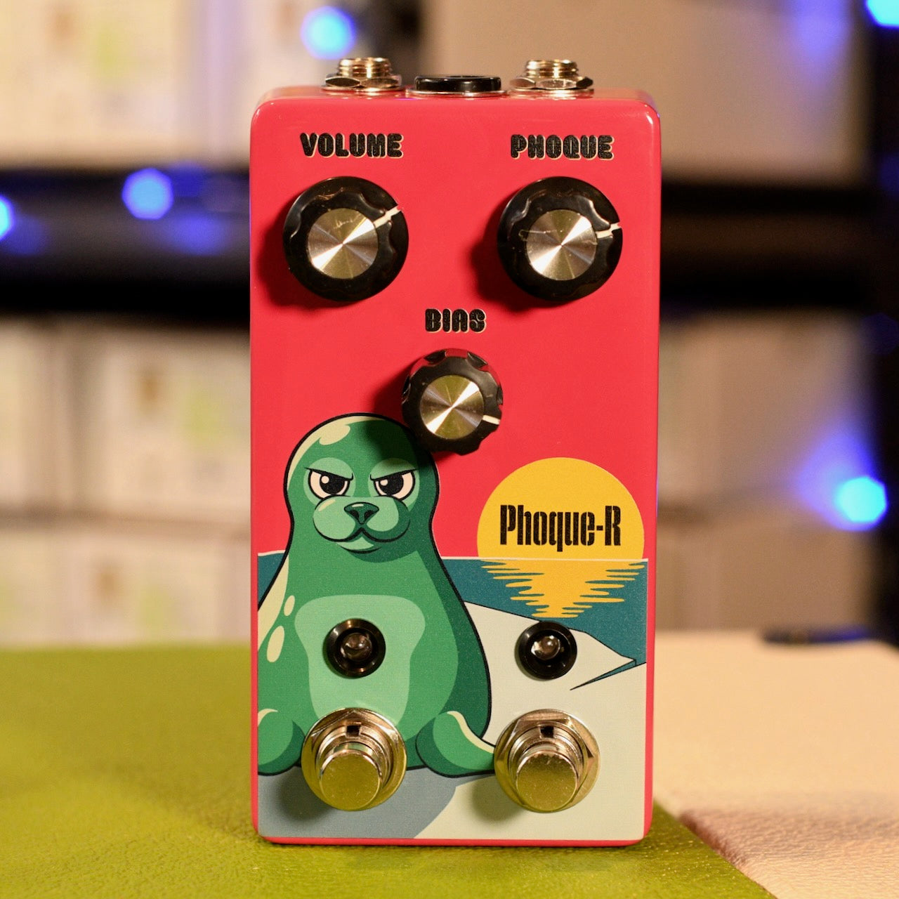 Red guitar pedal with green seal illustration, three knobs, two toggle switches, and two foot switches