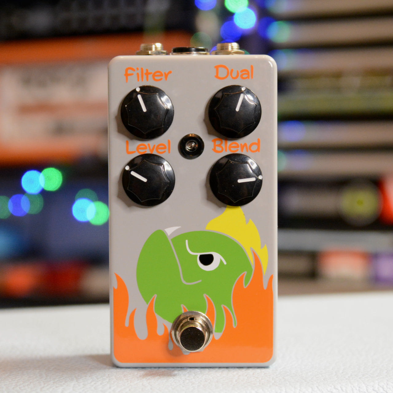 Gray guitar effects pedal with black knobs labeled filter, dual, level, and blend, and a green fish design with orange flames.