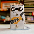 Silver guitar effects pedal with two black knobs, toggle switch, footswitch, and orange pliers graphic labeled 'TONE'
