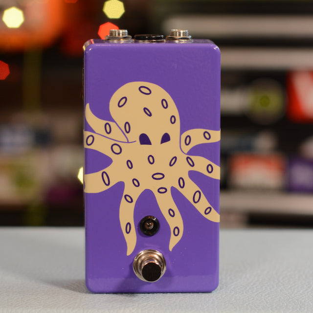 Purple metal pedal with beige octopus graphic, one footswitch, and two jack connectors on top.