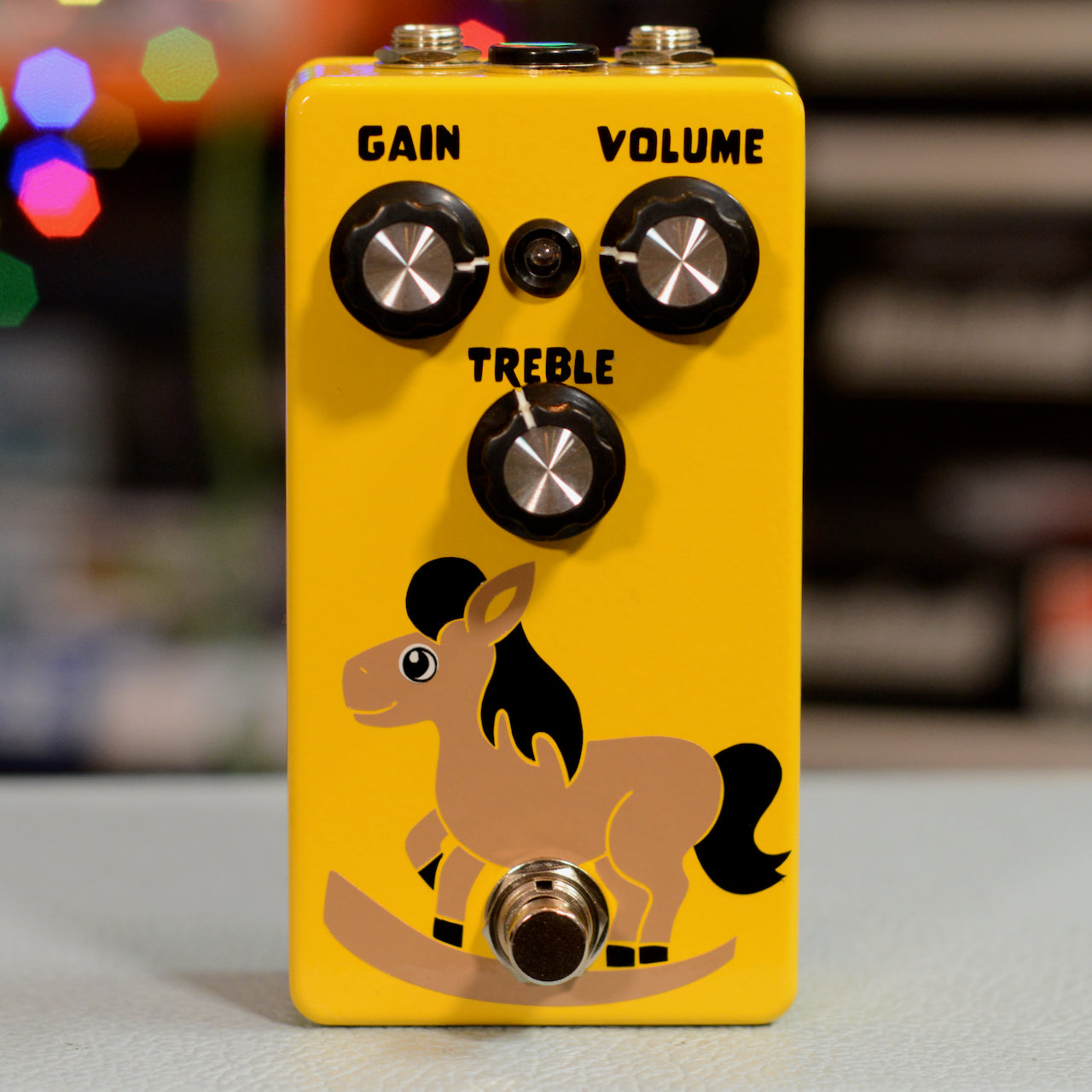 Yellow guitar effects pedal with three knobs labeled Gain, Volume, Treble and a rocking horse graphic.
