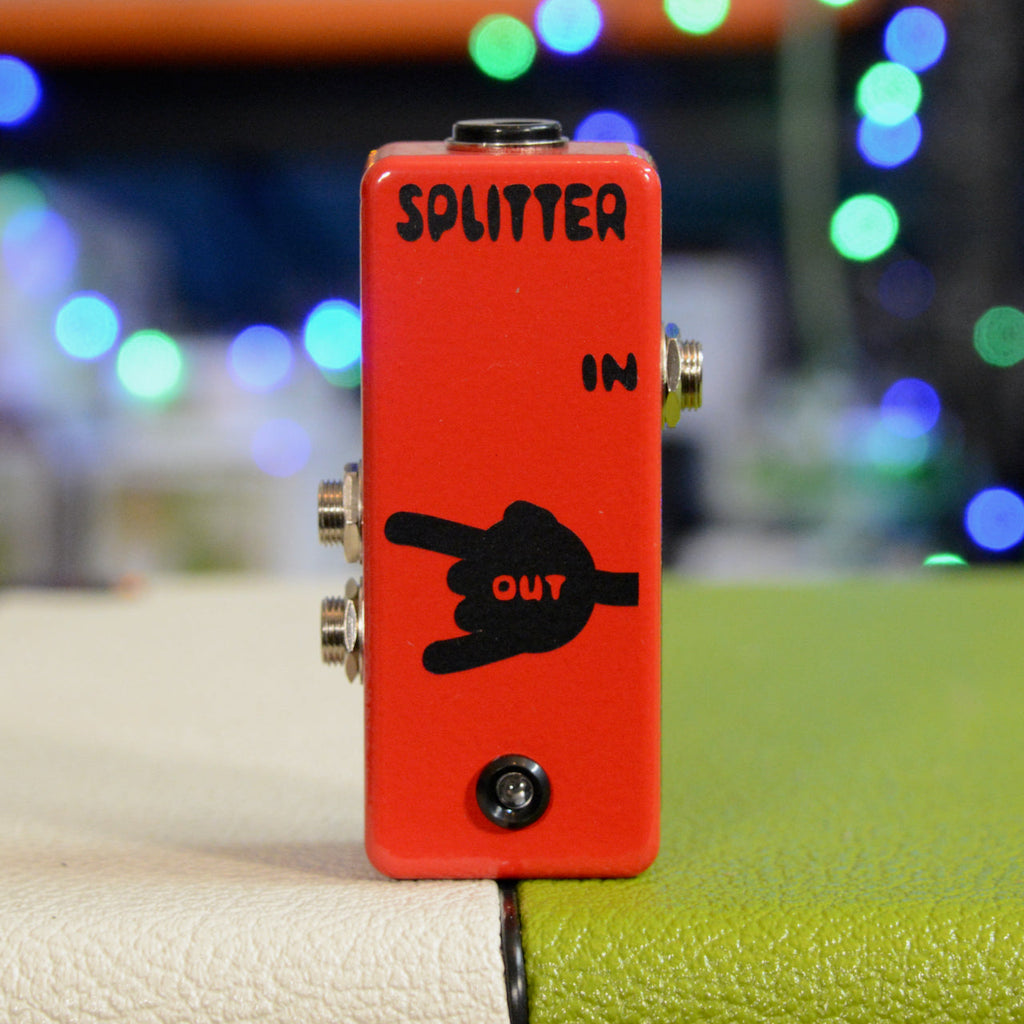 Red audio splitter box with three quarter inch jacks and one DC power input on a textured surface.
