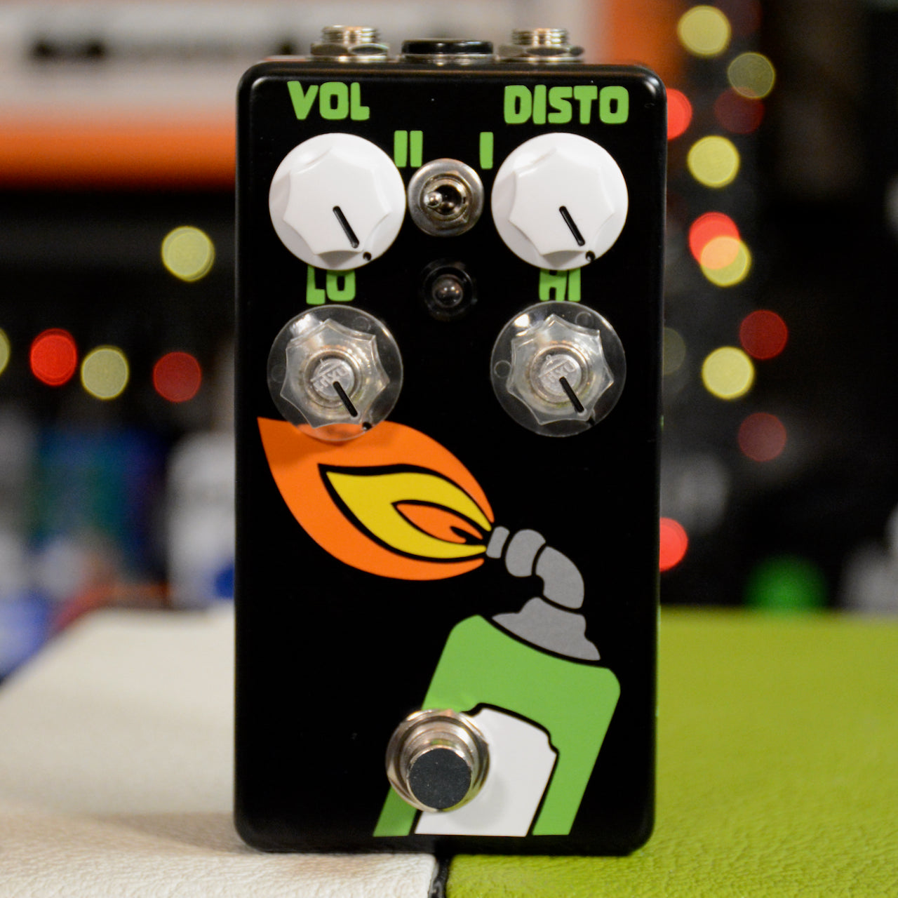 Black guitar effects pedal with green, orange, and yellow torch flame graphic, four knobs, a toggle switch, and a footswitch.