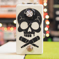 White guitar effects pedal with black skull and crossed cable graphics, one knob, and one footswitch.