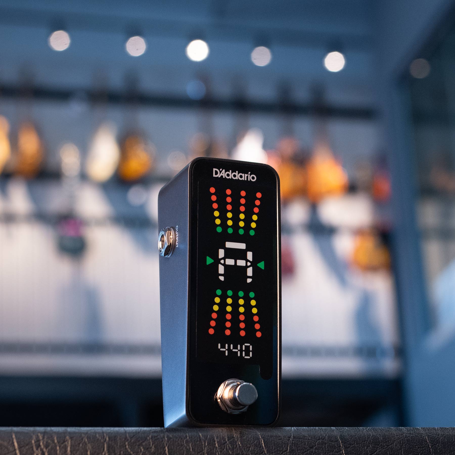 Black D'Addario pedal tuner with LED display and a footswitch, placed on a surface indoors.