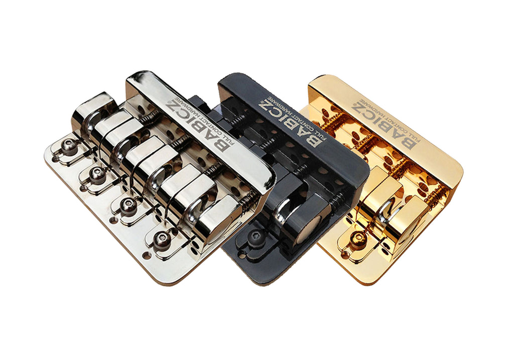 Three Babicz bass guitar bridges in silver, black, and gold finish shown side by side.