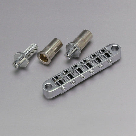Silver-colored metal Tune-o-matic style guitar bridge with two threaded bushings and a bridge post on gray background.